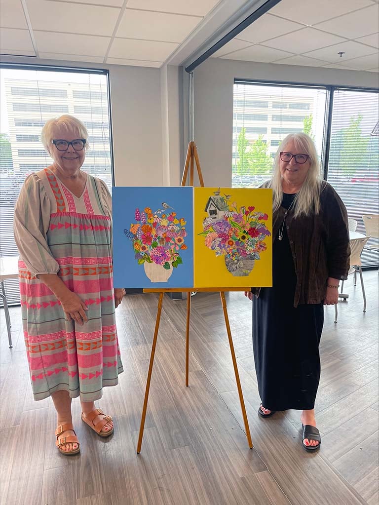 two senior woman standing next to art work